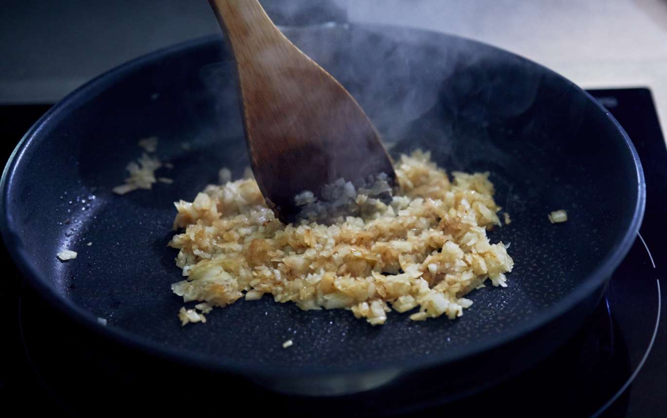 玉ねぎをみじん切りにし、油をひいて弱火で熱したフライパンに入れる。ひとつまみの塩をふり、色づくまで炒めたら、粗熱をとる。
